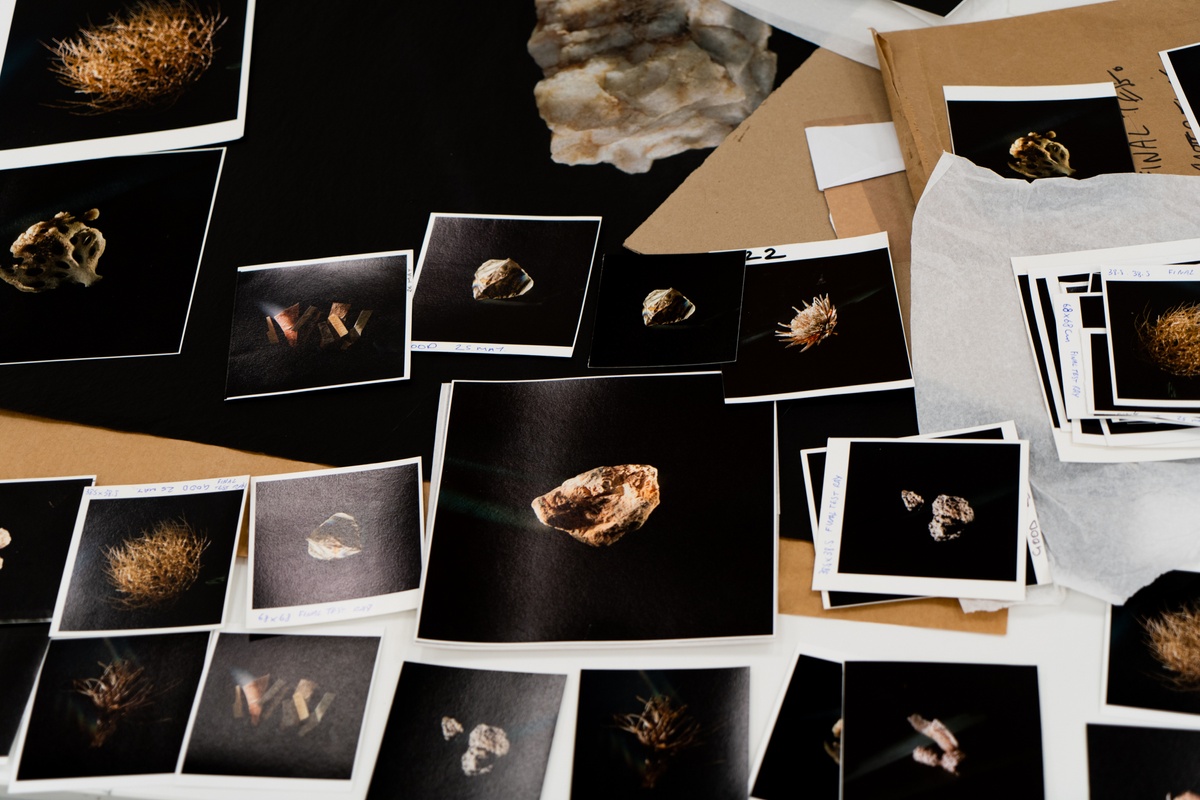 A process photograph from Tommaso Fiscaletti and Hemel Liggaam's residency at A4 Arts Foundation, showing the unpacking of their archive. Numerous small photographic prints are arranged on a table.
