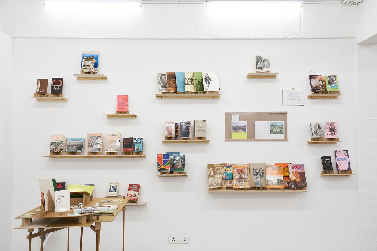 Installation photograph from the Papertrails exhibition in A4’s Reading Room. On the left, a wooden table with printed matter. At the back, various wall-mounted shelves with printed matter.
