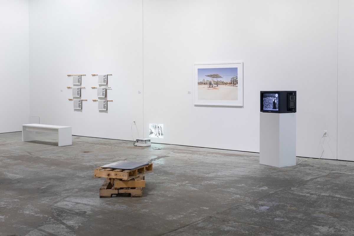 Installation photograph from ‘Crossing Night: Regional Identities x Global Context’ exhibition at the Museum of Contemporary Art Detroit. At the front, Edson Chagas’ installation ‘Found not taken’ sits on the gallery floor. On the left, Pieter Hugo’s photographic series and text ‘The Journey’ in the form printed newspaper booklets are hung on the wall. In the middle, Samson Kambalu’s video ‘I Take my Place in History’ is projected low on the wall, and Margaret Courtney Clarke’s photograph ‘Petrol Pump, Sesfontein, Namibia’ is mounted on the wall. On the right, Robin Rhode’s video ‘The Moon is Asleep’ is displayed on a screen sitting on a plinth.
