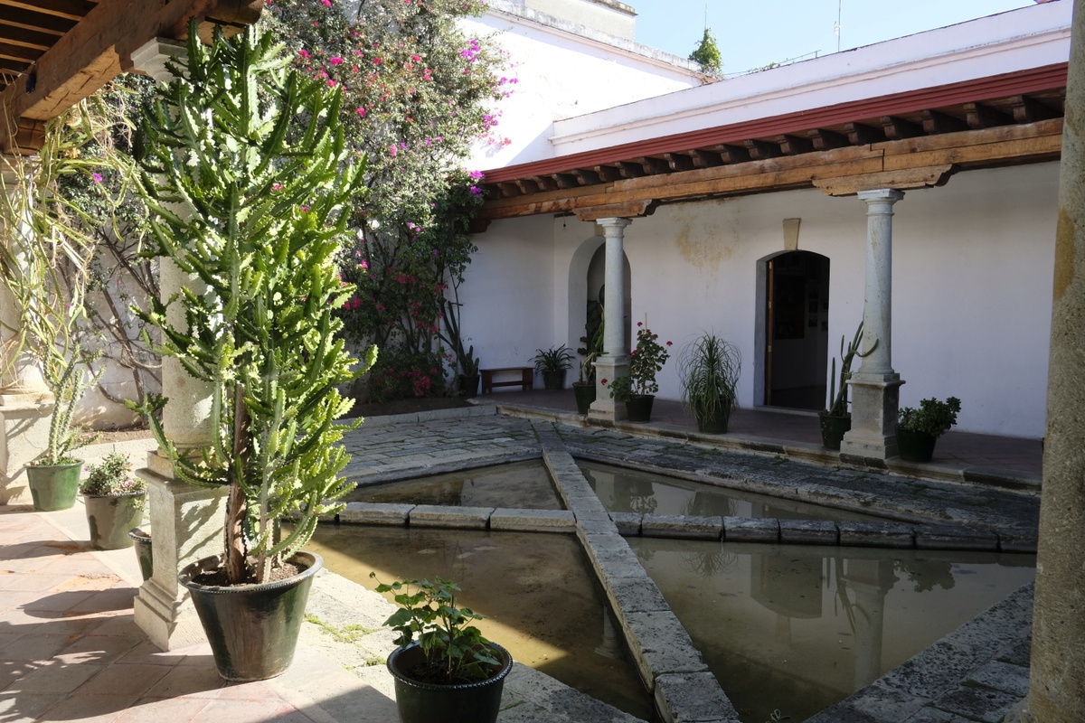 Ephemera from the series of offsite exhibitions ‘Crossing Night / Hacer Noche’ in Oaxaca, Mexico. A photograph shows a stone courtyard with a water feature.
