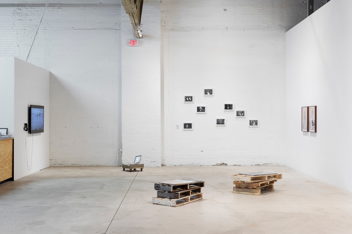 Installation photograph from ‘Crossing Night: Regional Identities x Global Context’ exhibition at the Museum of Contemporary Art Detroit. At the front, Edson Chagas’ photograph and wooden pallet installation ‘Found, not taken’ sits on the gallery floor. At the back, multiple monochrome photographs by Musa N. Nxumalo are mounted on the gallery wall.
