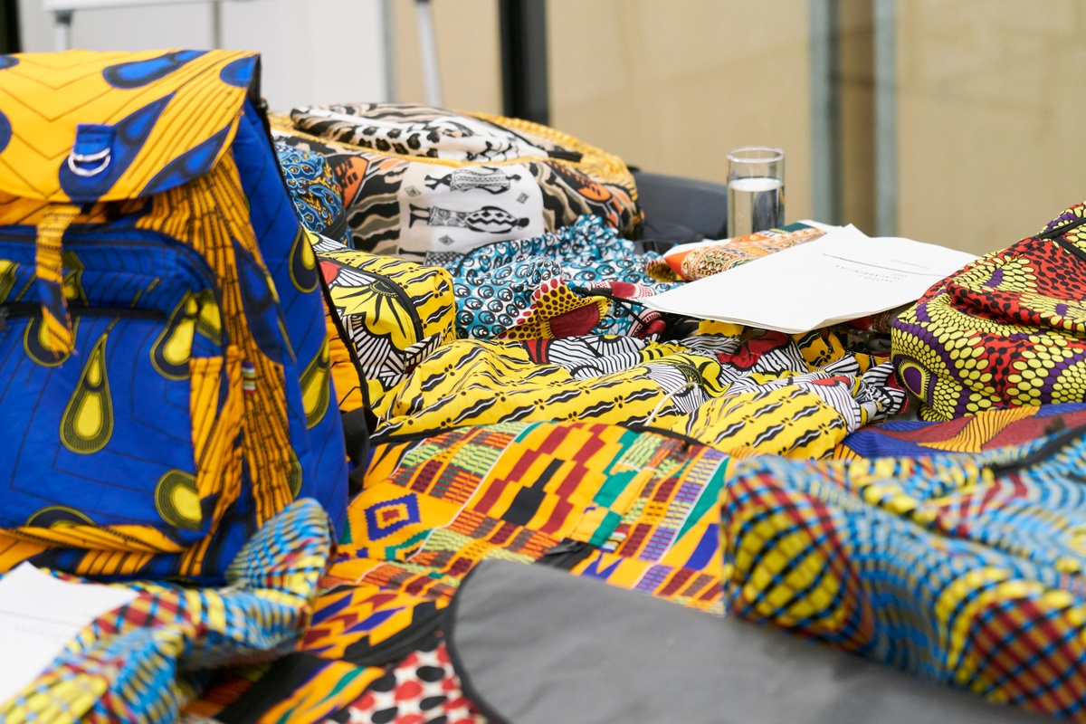 Event photograph from the Scalabrini Workshop that formed part of ‘Open Production’, Igshaan Adams’ hybrid studio/exhibition in A4’s Gallery. In the middle, a table laden is laden with backpacks that feature various prints.
