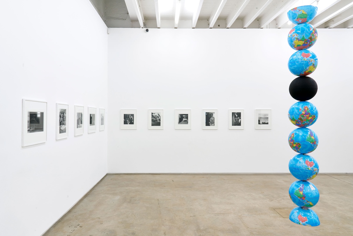 Installation photograph of the Common exhibition. To the right, Nolan Oswald Dennis’ ‘model for an endless column', a column of globe models, is suspended from the ceiling. One is solid black, the first and last are halved. On the left towards the back is Sabelo Mlangeni’s ‘Isivumelwano’.

