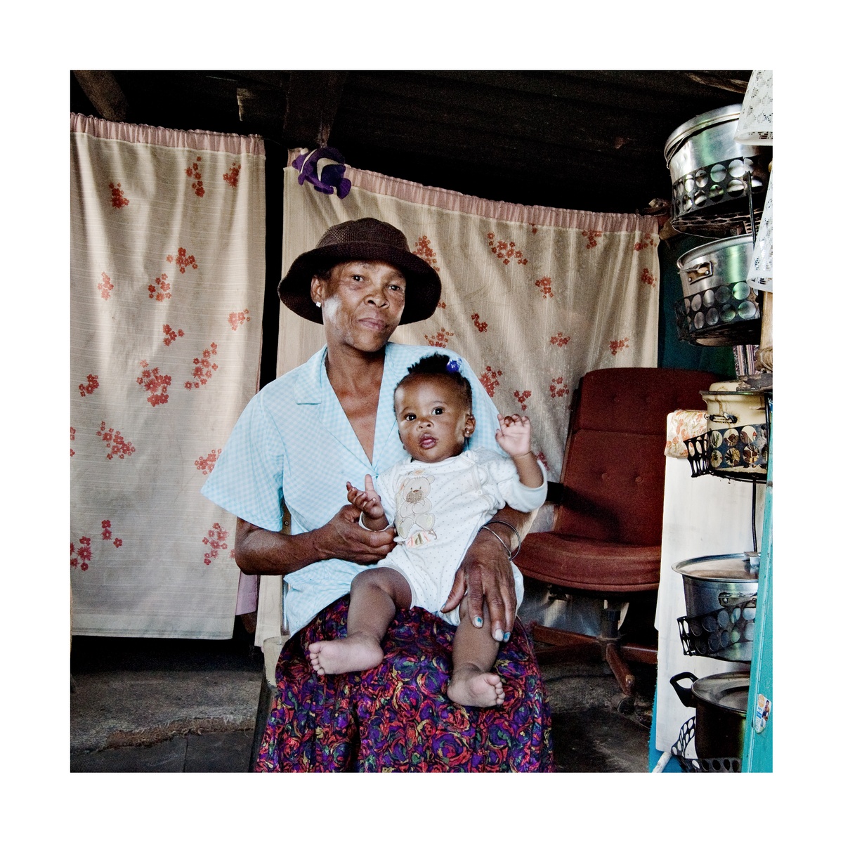 Photograph from Jabulani Dhlamini’s residency on A4’s top floor. At the back, curtains are strung across the room. At the front, a seated individual holds a baby.
