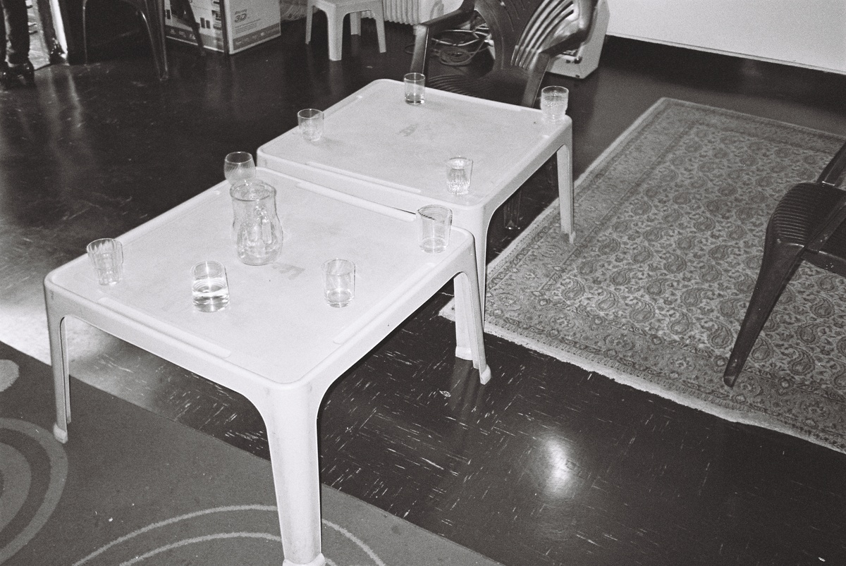 A photography from the Gladys' House workshop coordinated by Kemang Wa Lehulere in NY1, Guguletu shows two low plastic tables with water glasses surrounded by plastic chairs.
