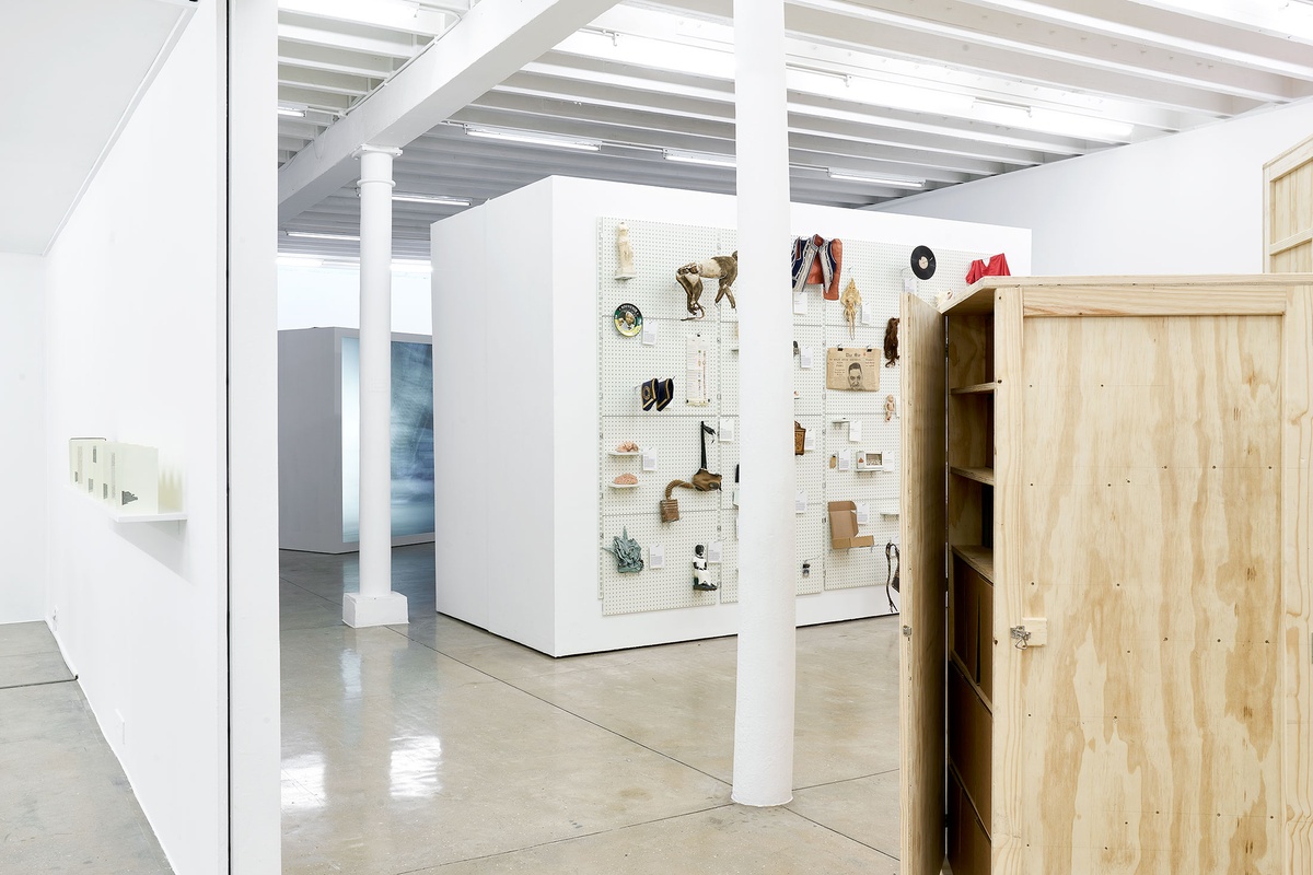 Installation photograph from the 'A Little After This' exhibition in A4 Arts Foundation's gallery. On the left, Colin Richards' Moleskin, collage and ink work 'A Little After This' is displayed on a wall-mounted shelf. On the right, collected objects from Penny Siopis' 'Will' work is mounted on a white moveable gallery wall through the use of perforated metal panels.
