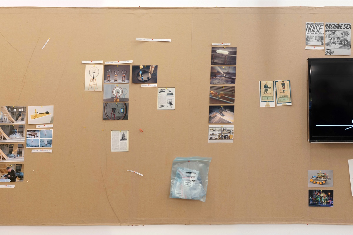 Installation photograph from Mitchell Gilbert Messina's residency in A4 Art Foundation. A wall-mounted strip of cardboard hosts pinned research notes.
