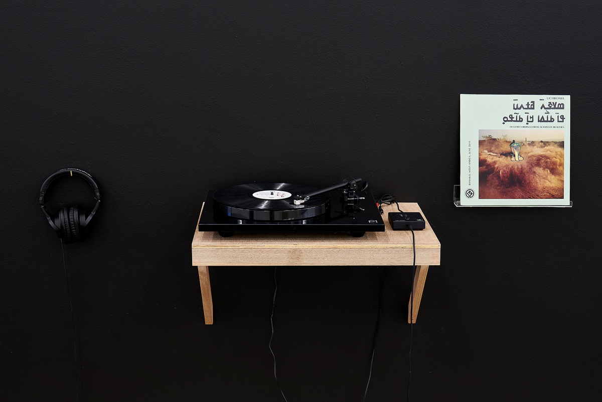 Installation photograph from the ‘Sounding the Void, Imaging the Orchestra V.1’ exhibition in A4’s Gallery that shows a vinyl record player on a wall-mounted shelf with headphones and records provided by the Sahel Sounds label.
