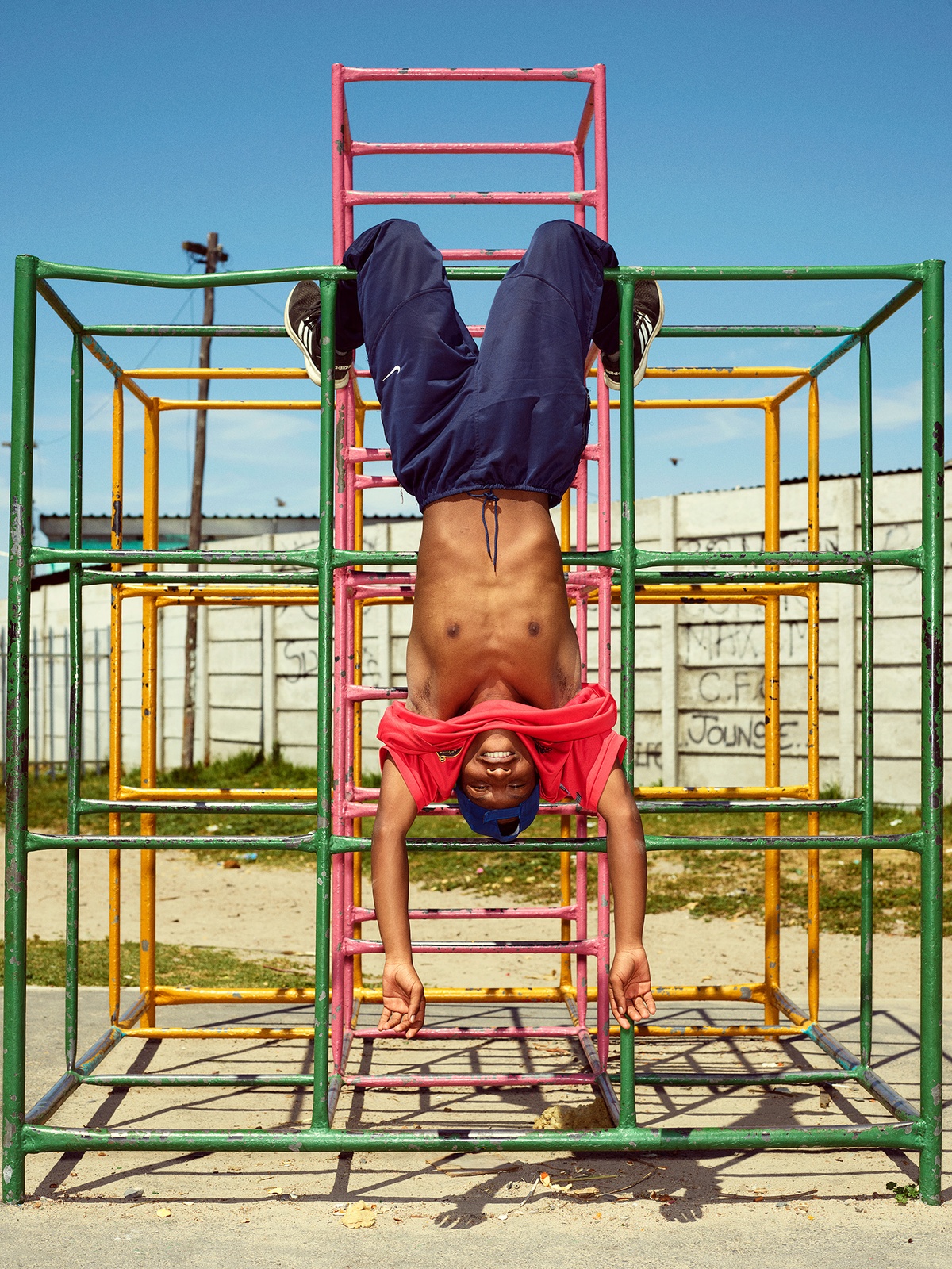 Photograph by Pieter Hugo, from A4’s ‘Atlantis Project’ exchange with the SWAGG United Dance Crew, that depicts a young person hanging upside-down from a metal jungle gym. 
