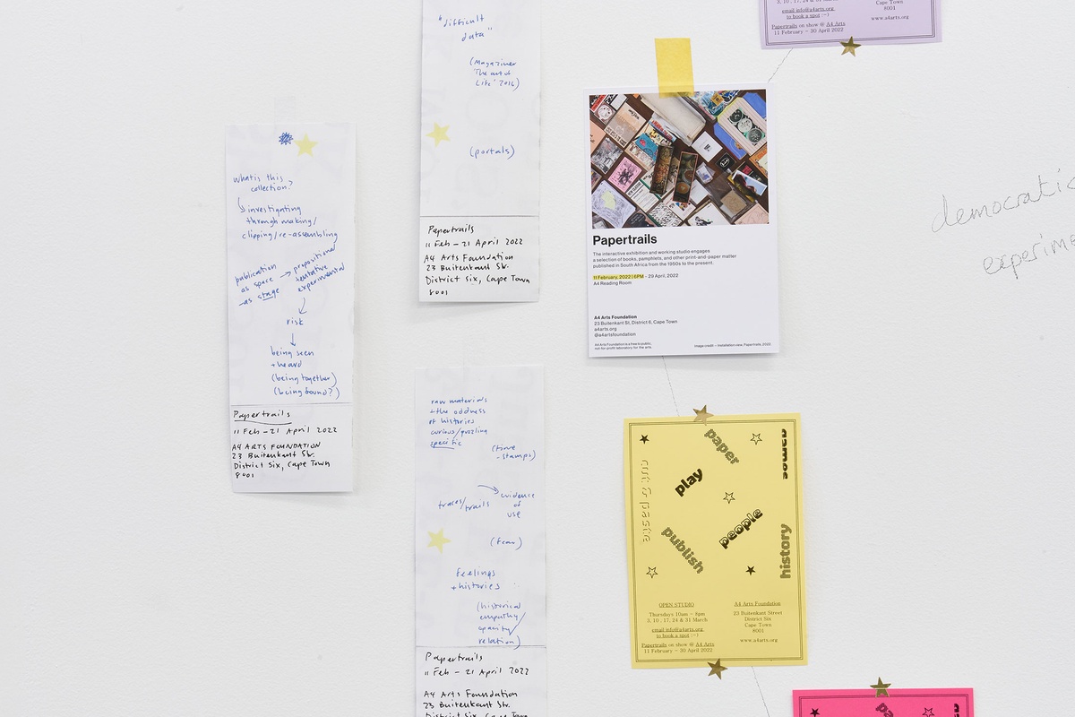 Installation photograph from the Papertrails exhibition in A4’s Reading Room. Handwritten notes and printed flyers for the exhibition are stuck onto a white wall.
