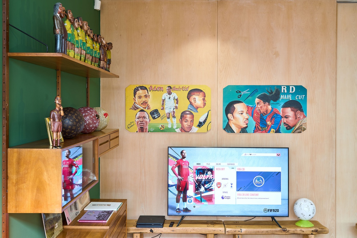 Installation photograph from the 2022 rendition of Exhibition Match on A4’s second floor. On the left, a wall-mounted wooden shelving unit hosts Mikhael Subotzky’s photograph ‘Self-Portrait with Soccer Team, Voorberg Prison’ and Johannes Segogela’s ‘Bafana Bafana Soccer Team’ sculpture. 
