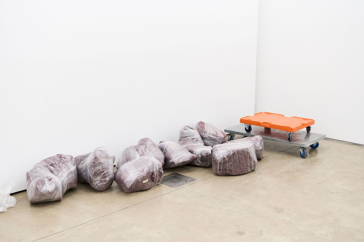 Process photograph from the 2nd rendition of ‘Parallel Play’ in A4’s Gallery. Sculptural objects by Kyle Morland wrapped in felt and bubble wrap are piled along the base of a white wall.
