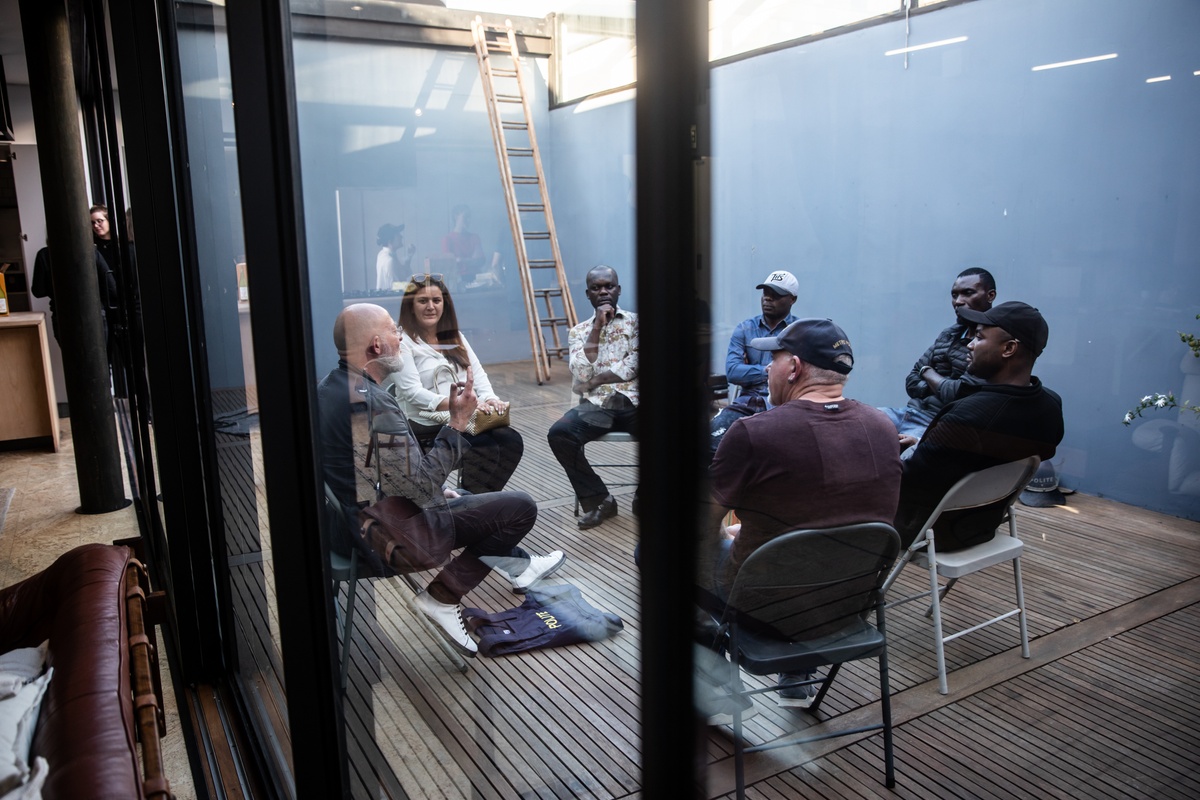 Process photograph from the 2019 rendition of Christian Nerf’s performance piece ‘Polite Force.’ Nerf and six participants are seated in circle on A4’s 2nd floor patio.
