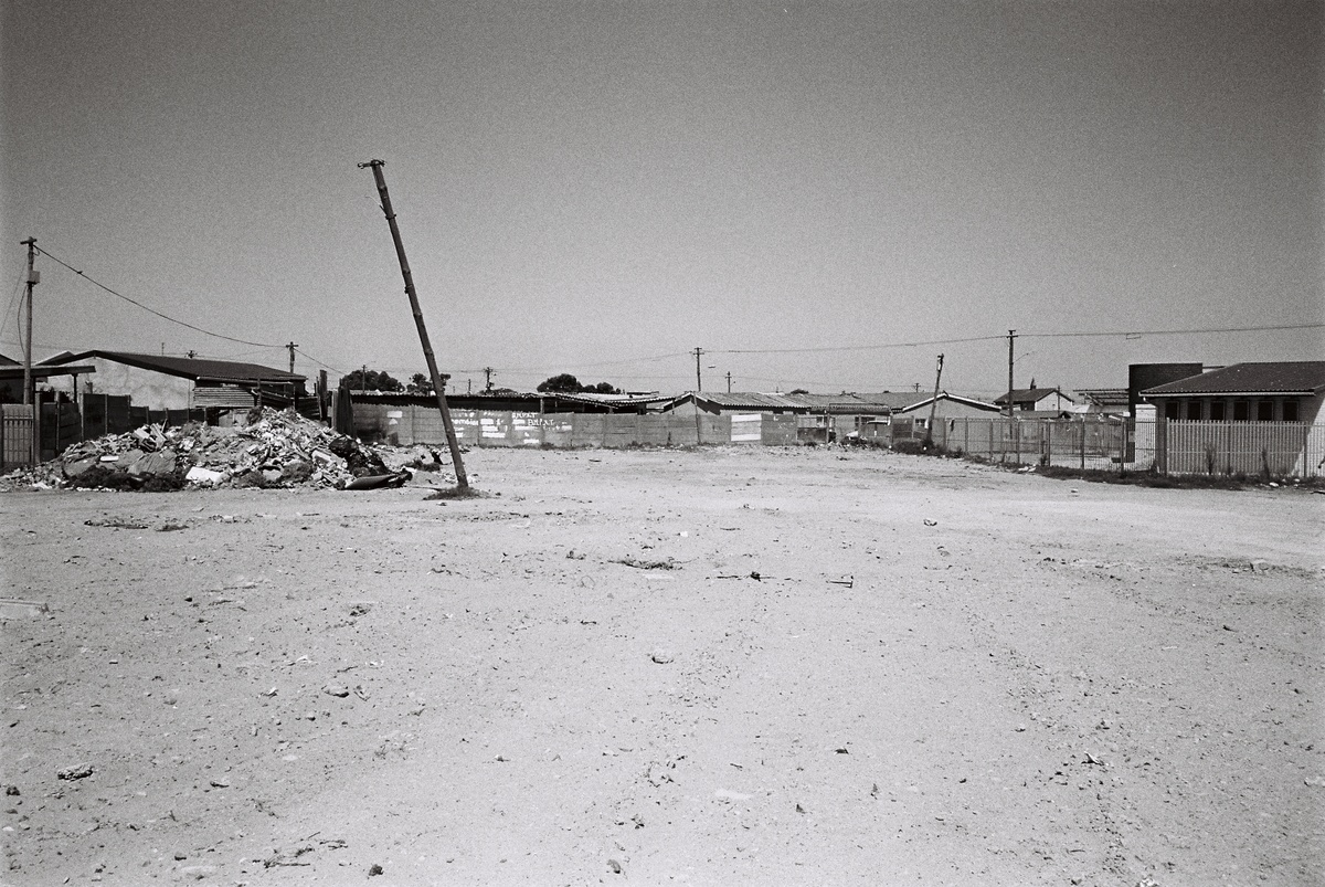 A photography from the Gladys' House workshop coordinated by Kemang Wa Lehulere in NY1, Guguletu shows a dirt plain demarcated by concrete and metal fencing.
