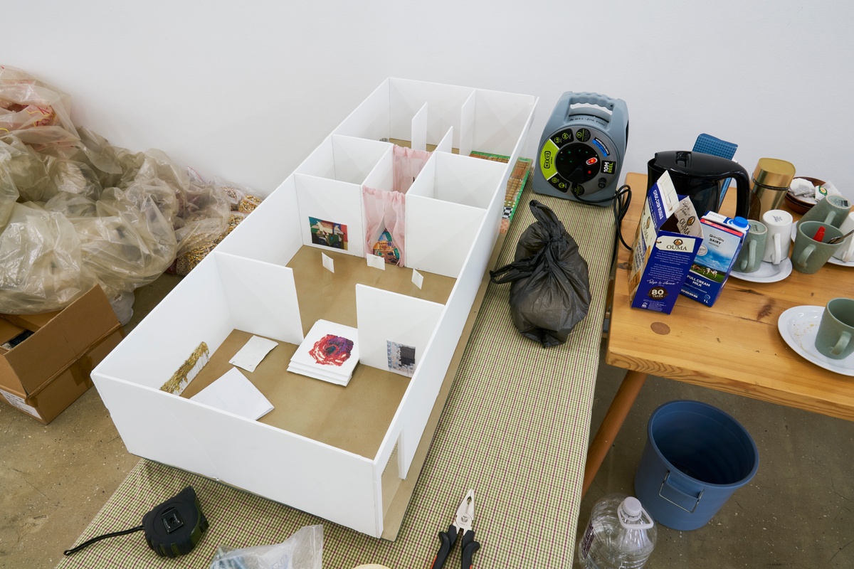 Process photograph from ‘Open Production’, Igshaan Adams’ hybrid studio/exhibition in A4’s Gallery. A small hardboard model of A4’s gallery with reproductions of Adams’ works sits on a table.

