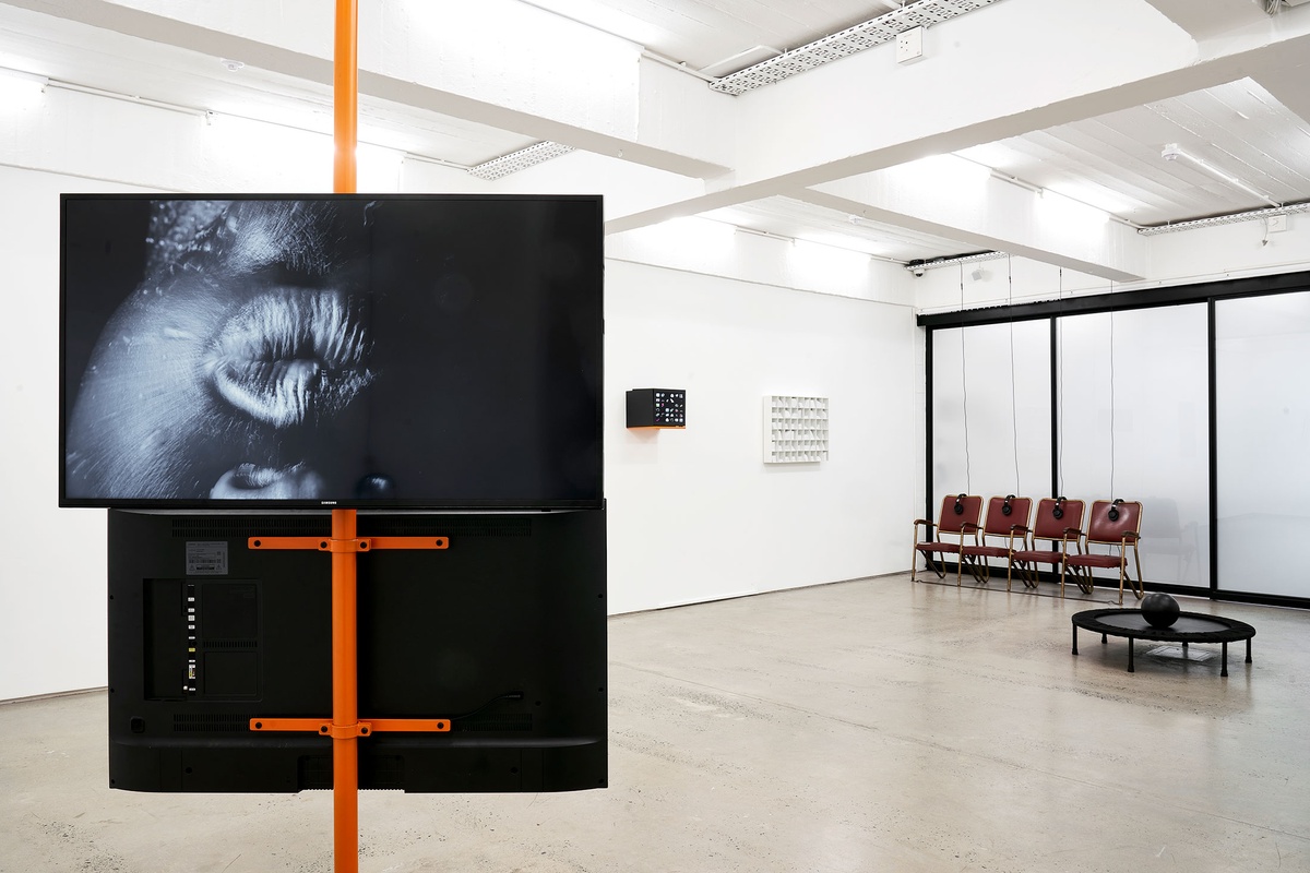 Installation photograph from the ‘Model’ exhibition in A4’s Reading Room. On the left, two counter facing screens are mounted a support beam, with Tony Yanick’s video ‘Make America Great Again (and again…and again)’ visible on one of them. 
