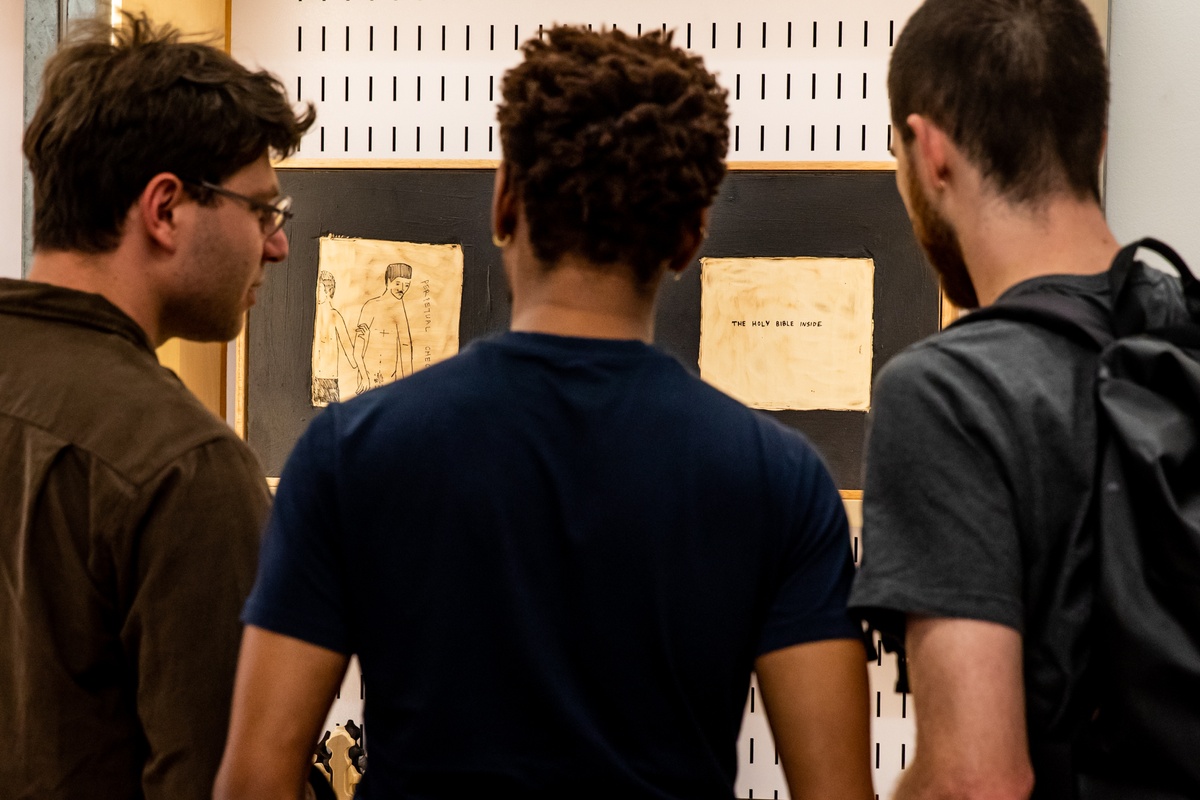 Event photograph from the launch of Brett Seiler’s chess set in A4’s Proto museum shop. At the back, a display cabinet holds Seiler's chess sets. At the front, three individuals observe the display.
