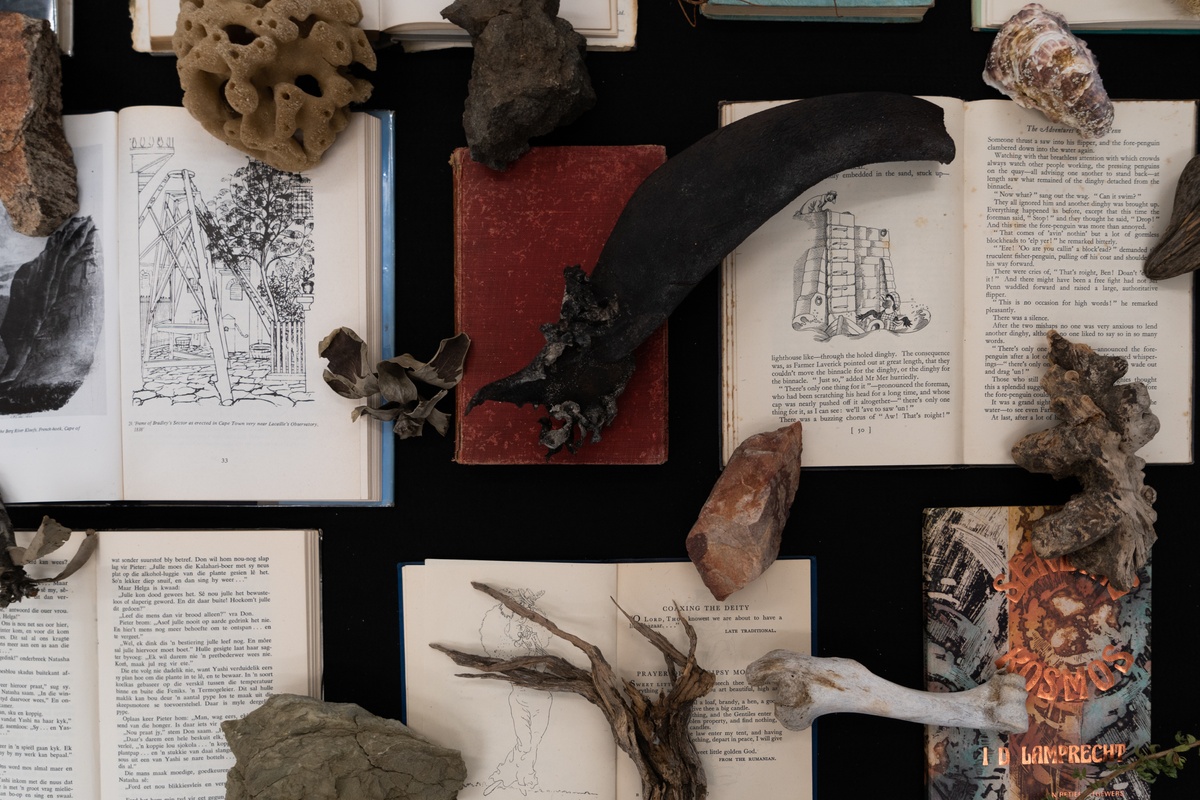 A process photograph from Tommaso Fiscaletti and Hemel Liggaam's residency at A4 Arts Foundation, showing the unpacking of their archive. A top-down view shows numerous books  and objects arranged on a felt-covered surface.
