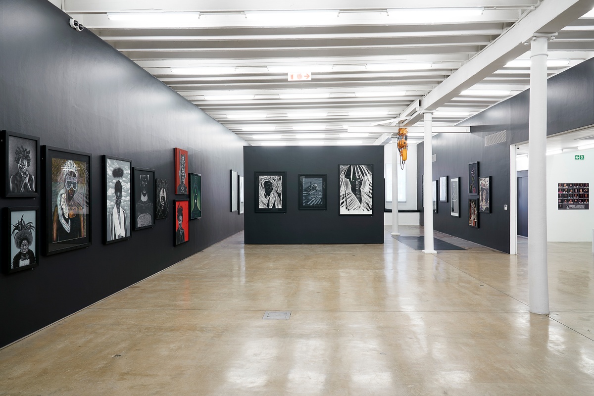Installation photograph from the “Ikhono LaseNatali” exhibition in A4’s Gallery. In the middle, a black moveable gallery wall lined with various artworks. On the left, the black gallery wall is lined with various artworks.
