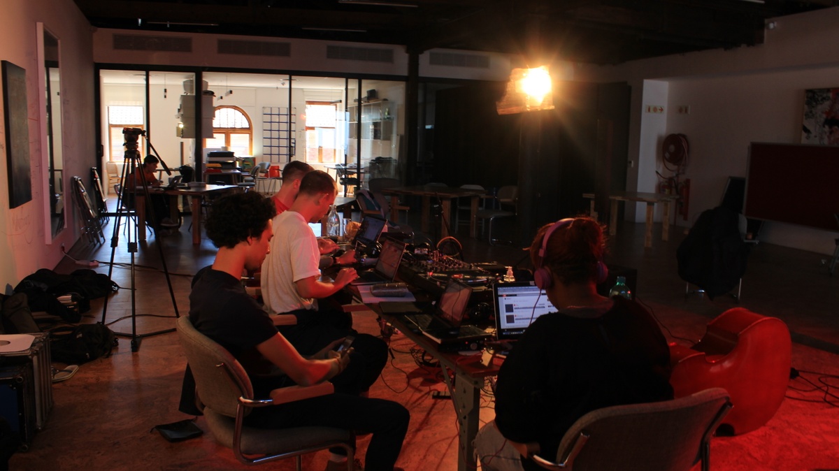 Process photograph from artists in residence Mushroom Hour Half Hour’s ‘re-vinylize’ sessions on A4’s top floor that shows their ‘open studio’ setup - a long wooden table laden with laptops and audio equipment. On the left, Shakeel Cullis, Dion Monti and Andrew Curnow. On the right, Naledi Chai.
