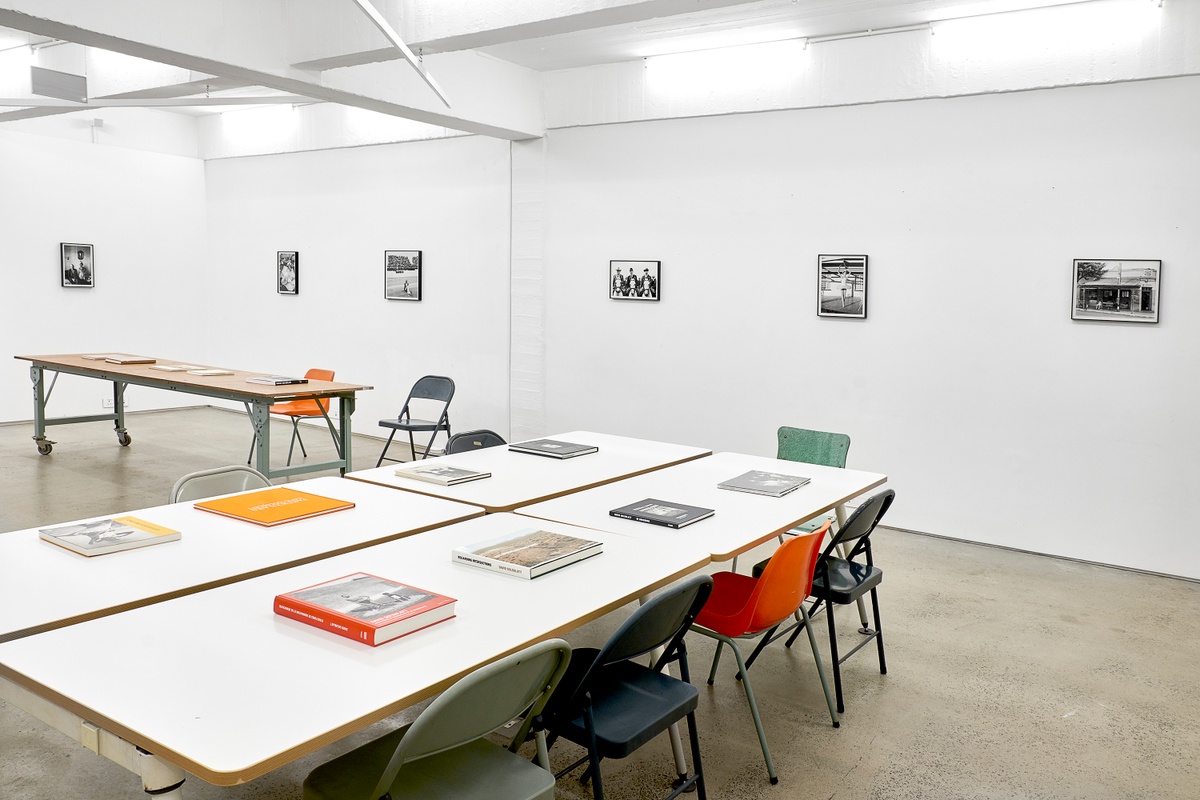 Installation photograph from the ‘Picture Theory’ exhibition in A4’s Gallery that depicts an installation in A4’s Library. At the back, David Goldblatt’s monochrome photographs are mounted on the wall. At the front, a selection of David Goldblatt’s photo-books are arranged on tables with with seating.
