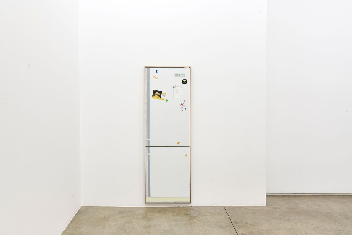 Installation photograph of the Common exhibition. Guy Simpson’s untitled life-sized acrylic painting of a refrigerator is hung on a white wall with the bottom of the painting nearly skirting the gallery floor.
