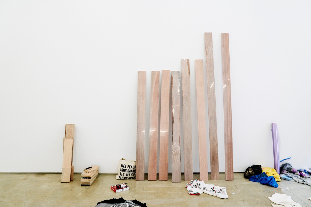 Process photograph from the ‘without a clear discernible image’ exhibition in A4’s Gallery, where the gallery was temporarily used as a studio space by the artist Kevin Beasley. In the middle, wooden planks of various lengths lean against the gallery wall.
