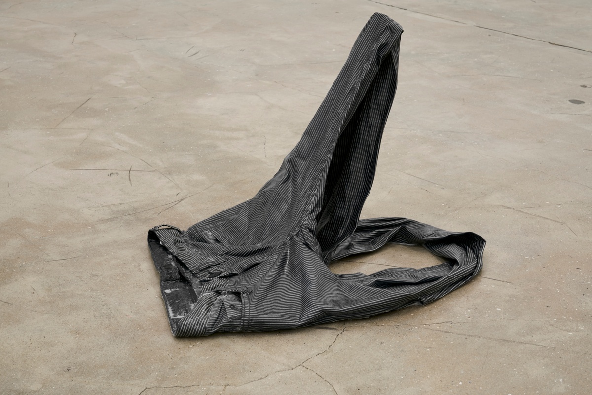 A photograph of Kevin Beasley's resin and trouser sculpture 'Knees' lying on a concrete floor.
