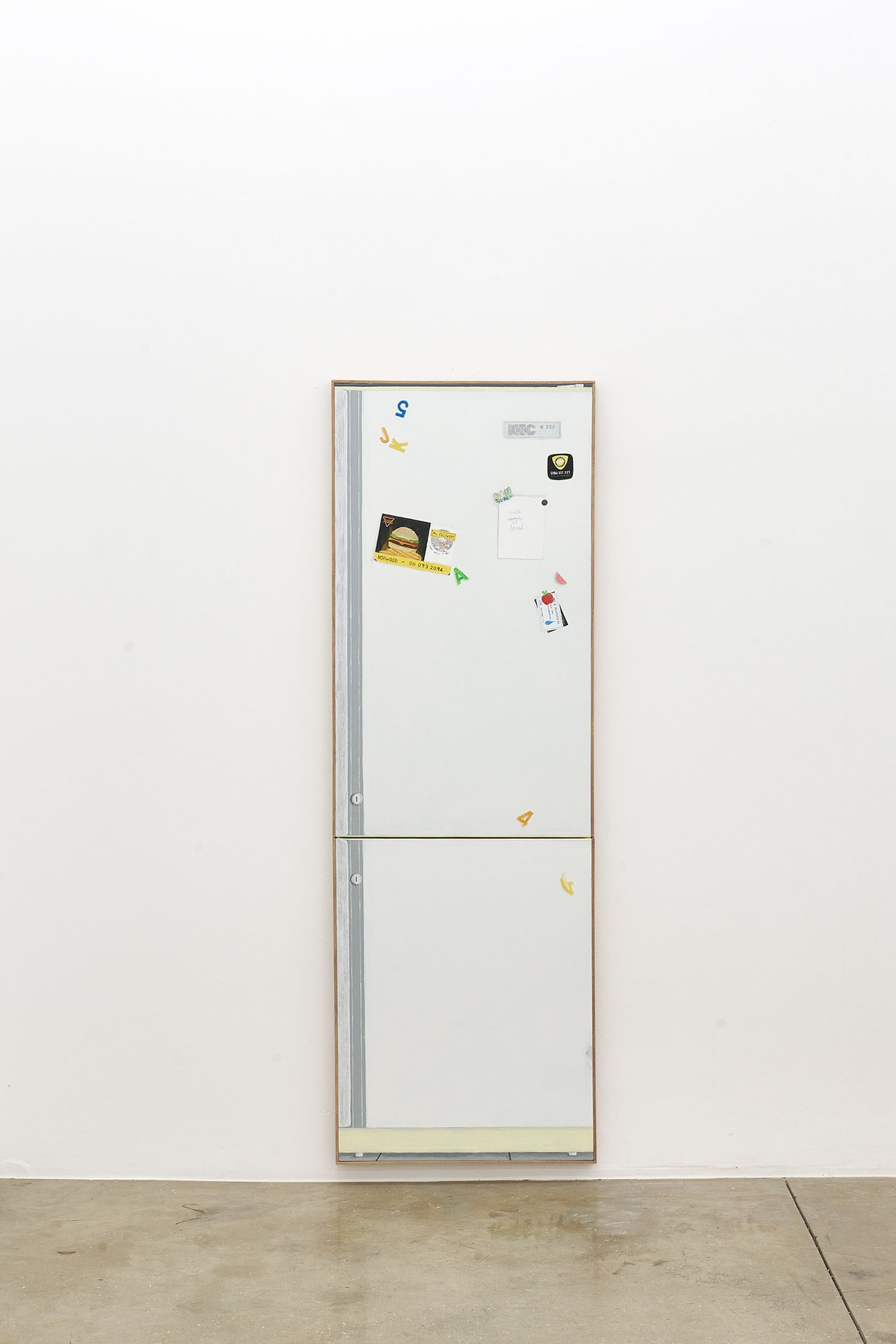 Installation photograph of the Common exhibition. Guy Simpson’s untitled life-sized acrylic painting of a refrigerator is hung on a white wall with the bottom of the painting nearly skirting the gallery floor.
