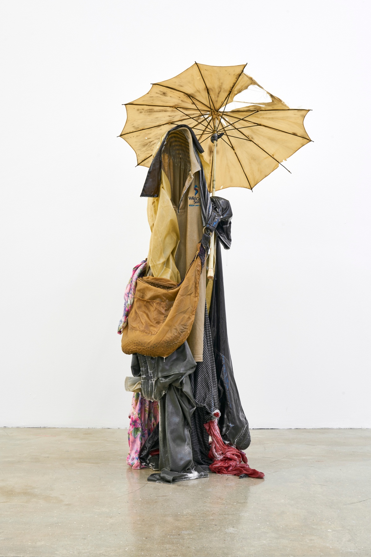 A photograph of Kevin Beasley's untitled resin, garment and umbrella sculpture standing on a concrete floor.
