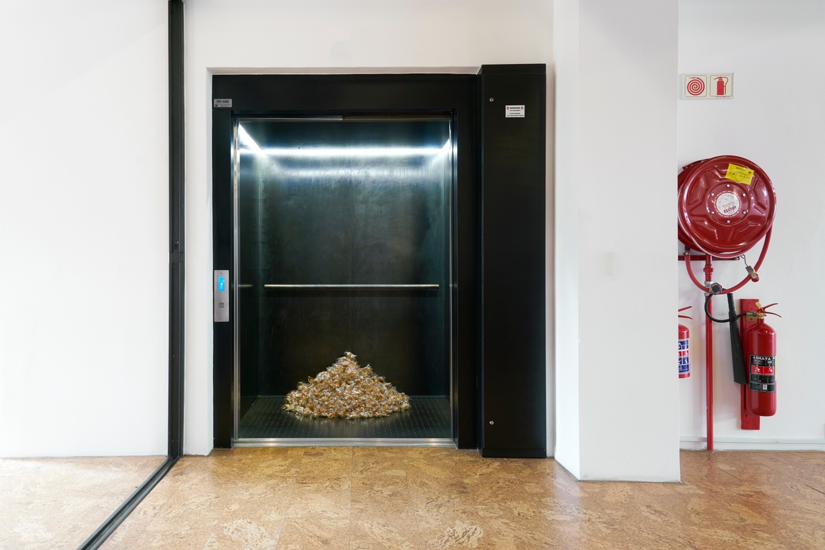 Installation photograph of Felix González-Torres' ‘Untitled (Fortune Cookie Corner)’ in A4’s elevator, with wrapped fortune cookies piled against the back of the interior.
