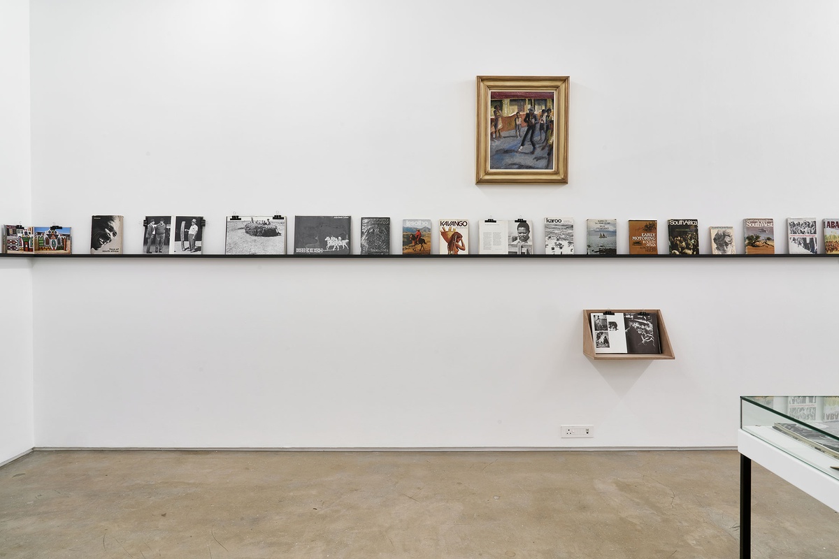 Installation photograph from the Photo Book! Photo-Book! Photobook! exhibition in A4’s Gallery. In the middle, Gerard Sekoto’s oil painting ‘Street Musician in District Six’ hangs above a display shelf in an area dedicated to photobooks from the years 1945 to 1967.
