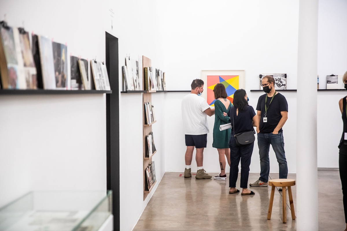Event photograph from the opening of the Photo Book! Photo-Book! Photobook! exhibition in A4’s Gallery in an area used to house photobooks from the years 1945 to 1967. Attendees converse in front of Albert Newall’s oil painting ‘Harmonic Development within a Square’.
