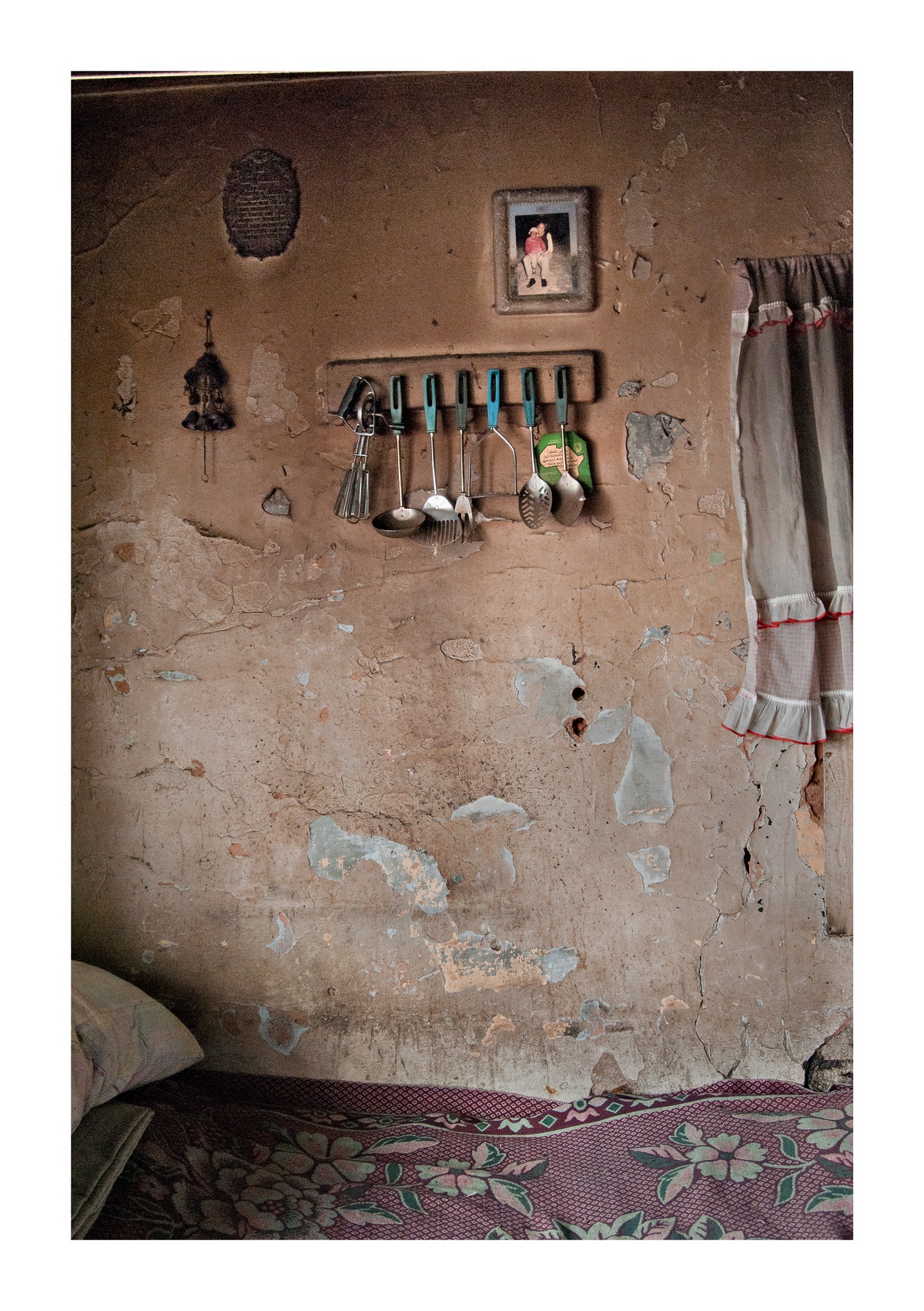 Photograph from Jabulani Dhlamini’s residency on A4’s top floor. At the top, a row of kitchen utensils on a wall-mounted utensil rack. At the bottom, a bed sits against the base of the wall.
