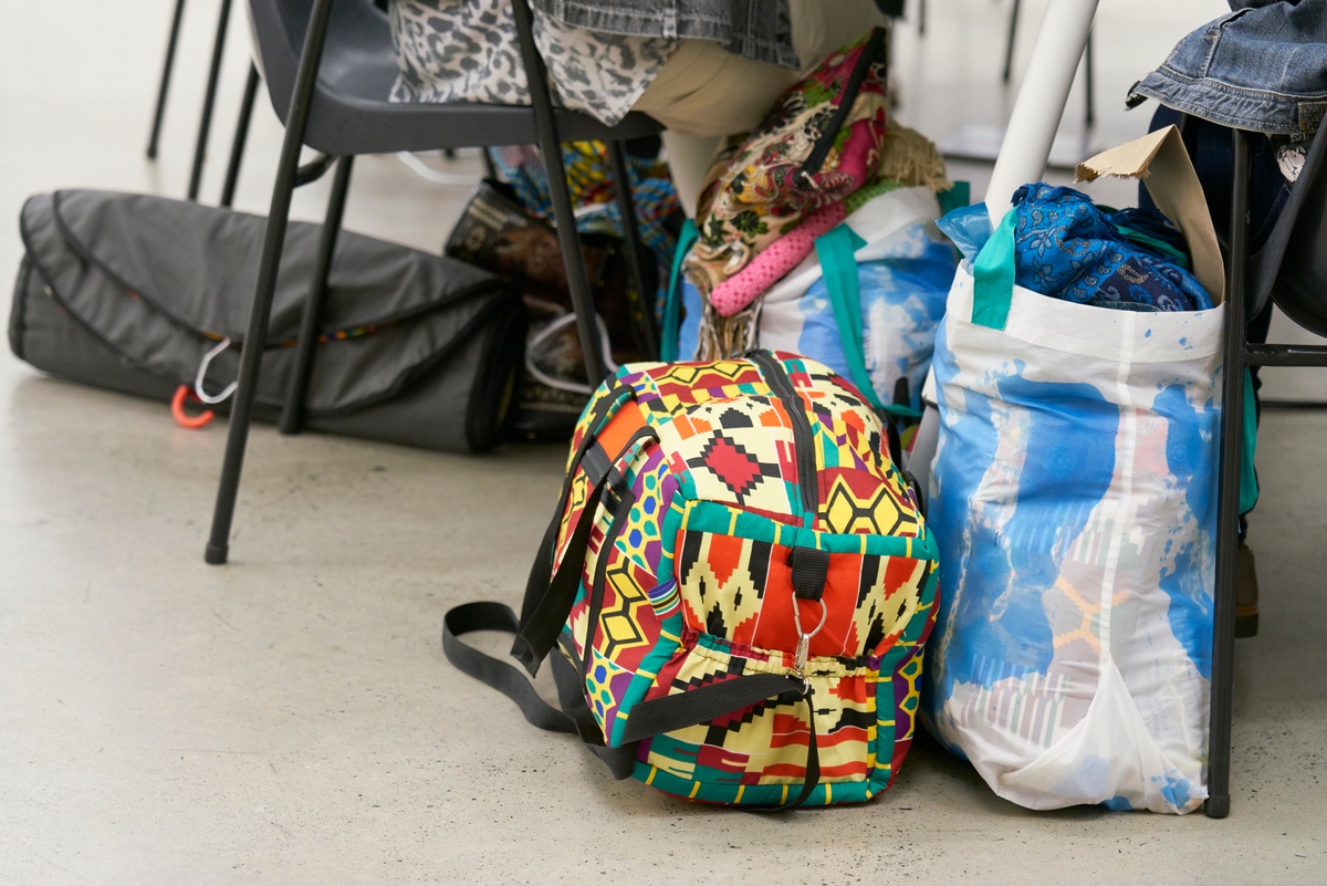 Event photograph from the Scalabrini Workshop that formed part of ‘Open Production’, Igshaan Adams’ hybrid studio/exhibition in A4’s Gallery. Bags holding fabrics sit on the floor next to chairs occupied by workshop attendees.
