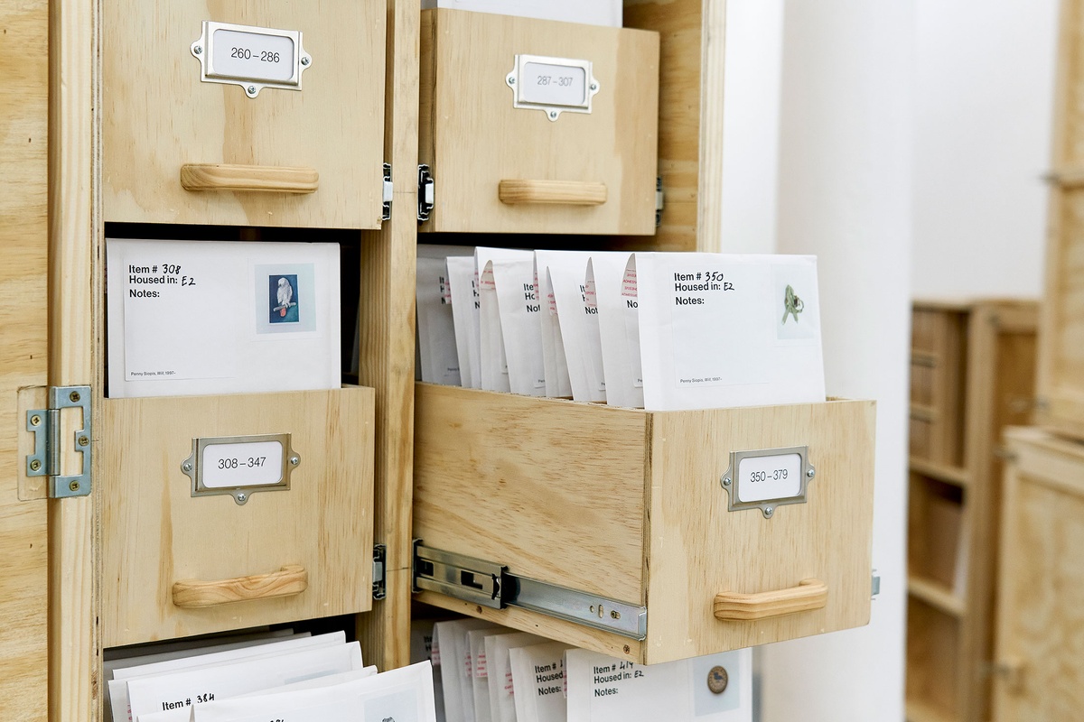 Installation photograph from the 'A Little After This' exhibition in A4 Arts Foundation's gallery that shows collected objects from Penny Siopis' 'Will' work organised in envelopes, which in turn are arranged in bespoke wooden filing cabinets.
