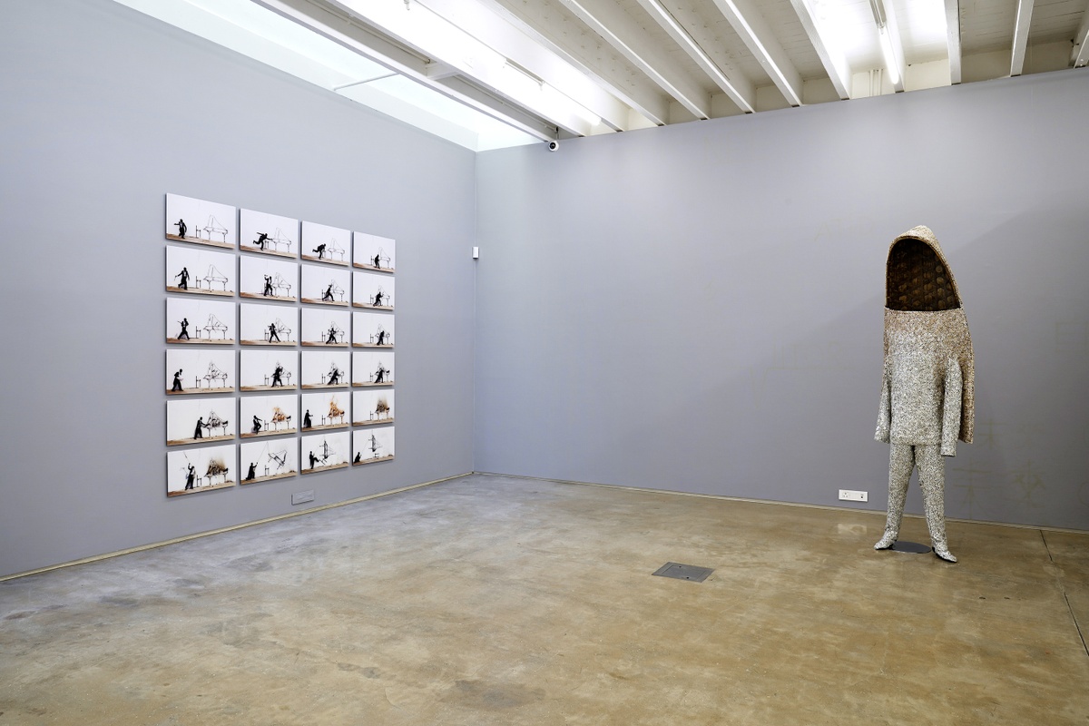 Installation photograph from the ‘Sounding the Void, Imaging the Orchestra V.1’ exhibition in A4’s Gallery. At the left, Robin Rhode’s photographic series ‘Piano Chair’ is mounted on the gallery wall. On the right, Nick Cave’s sculpture ‘Soundsuit’ stands on the gallery floor.
