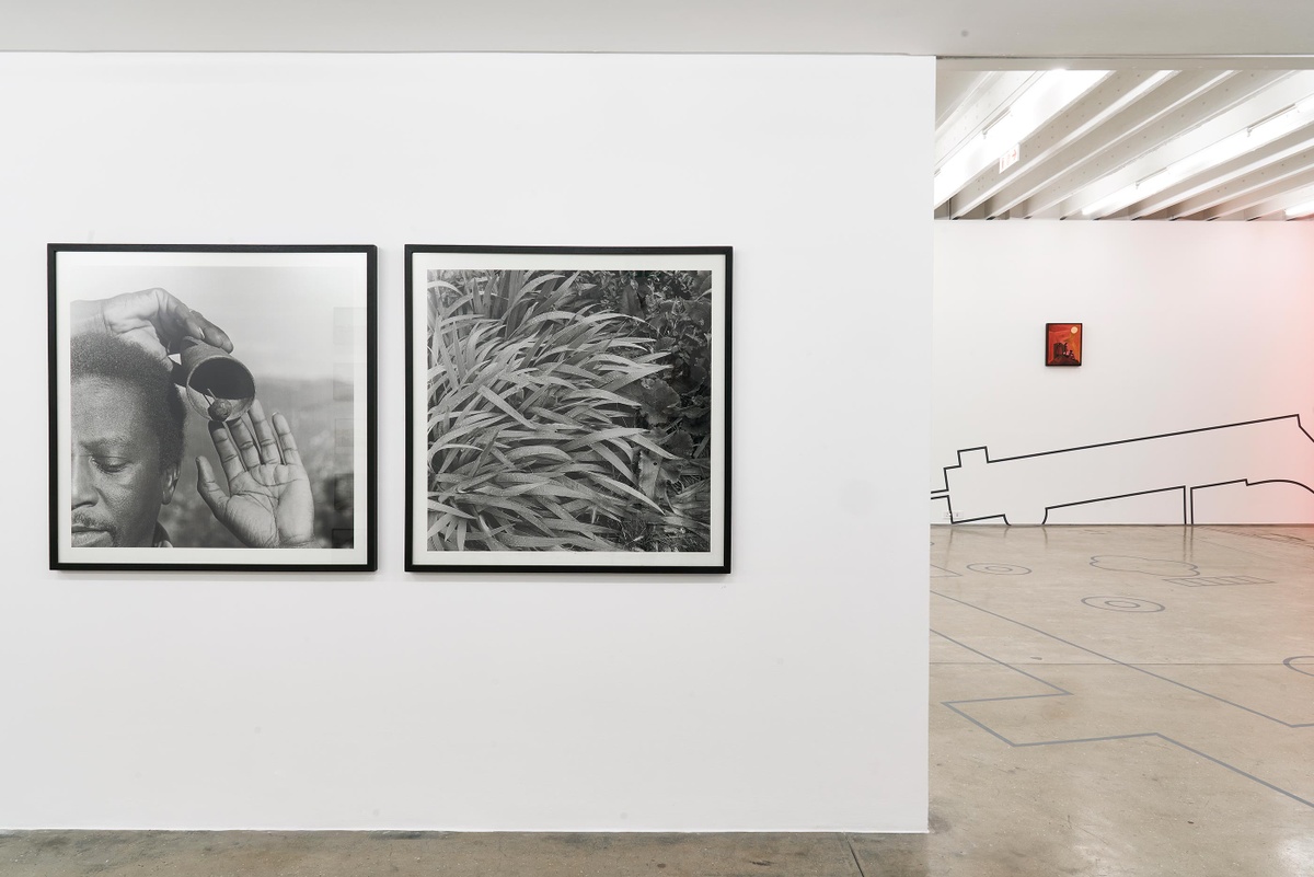 Installation photograph from the Customs exhibition in A4’s Gallery. On the left, George Hallett’s framed monochrome photographic diptych ‘Peter Clarke’s Tongue’ is mounted on a white gallery wall. On the right, Peter Clarke’s painting ‘Anxiety’ is mounted on a gallery wall that also features part of Dor Guez’s vinyl wall installation ‘Double Stitch’.
