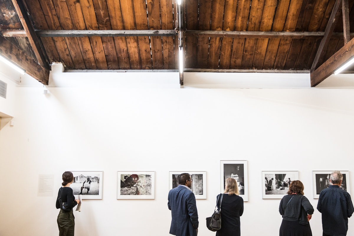 Event photograph from the launch of Omar Badsha’s book ‘Seedtimes’ on A4’s top floor. At the back, a row of Omar Badsha’s monochrome photographs are mounted on the wall. At the front, attendees look at the photographs.
