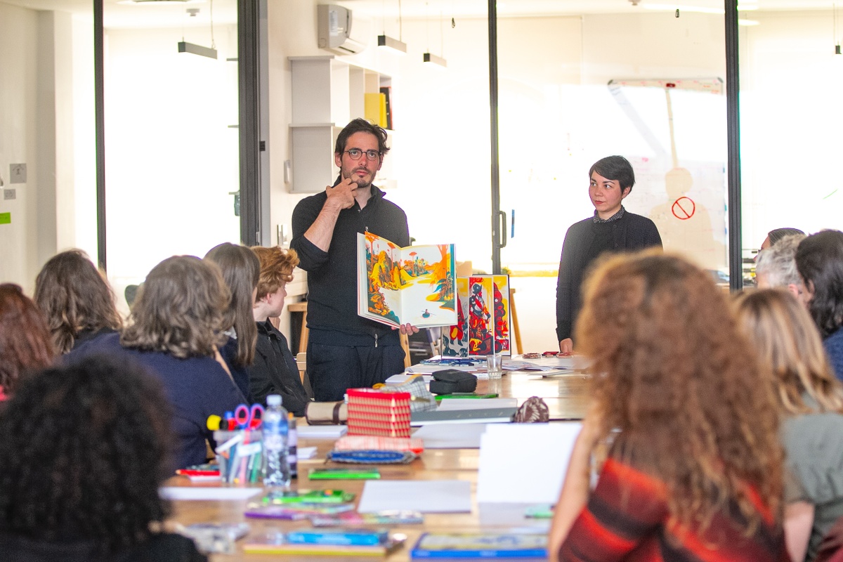 Event photograph from the 2018 rendition of the Open Book festival on A4’s ground floor that depicts the Cencertina Books Workshop on A4’s top floor. At the front, attendees are seated along a table. At the back, Raphael Urwiller and Mayumi Otero from Icinori.
