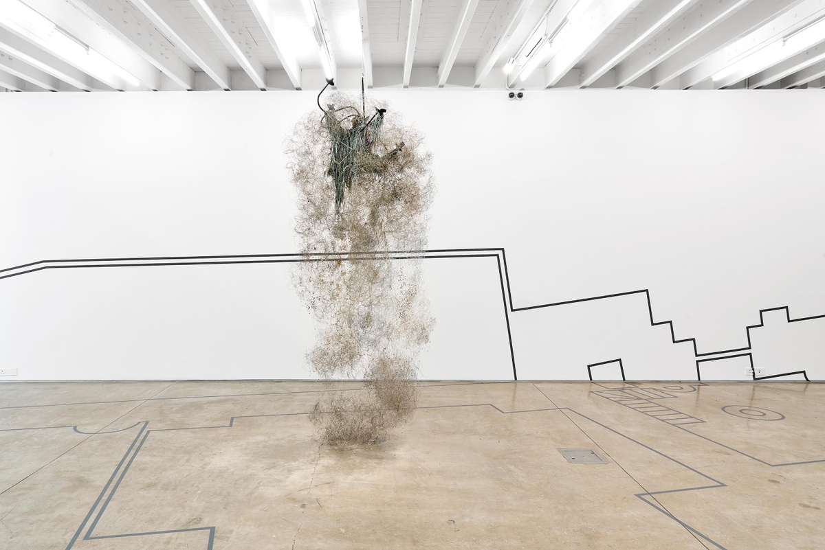 Installation photograph of Igshaan Adams’ wire, chain, chandelier and bead sculpture ‘65 Bloem Street’, from the ‘Customs’ exhibition in A4’s Gallery, which shows the sculpture suspended from the gallery ceiling.
