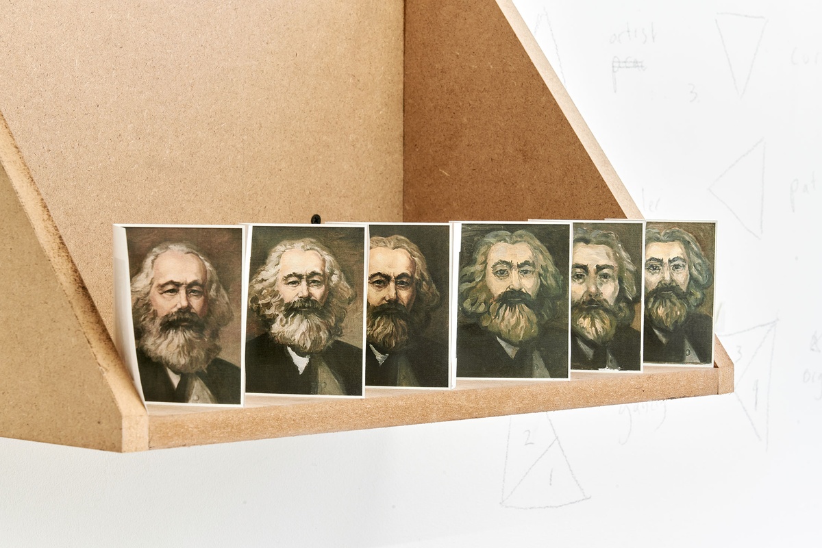 Process photograph from Patrick Waterhouse's 2022 residency in A4 Arts Foundation's studio shows a closeup view of a paper accordion with photographic prints arranged on a wooden wall-mounted shelf.
