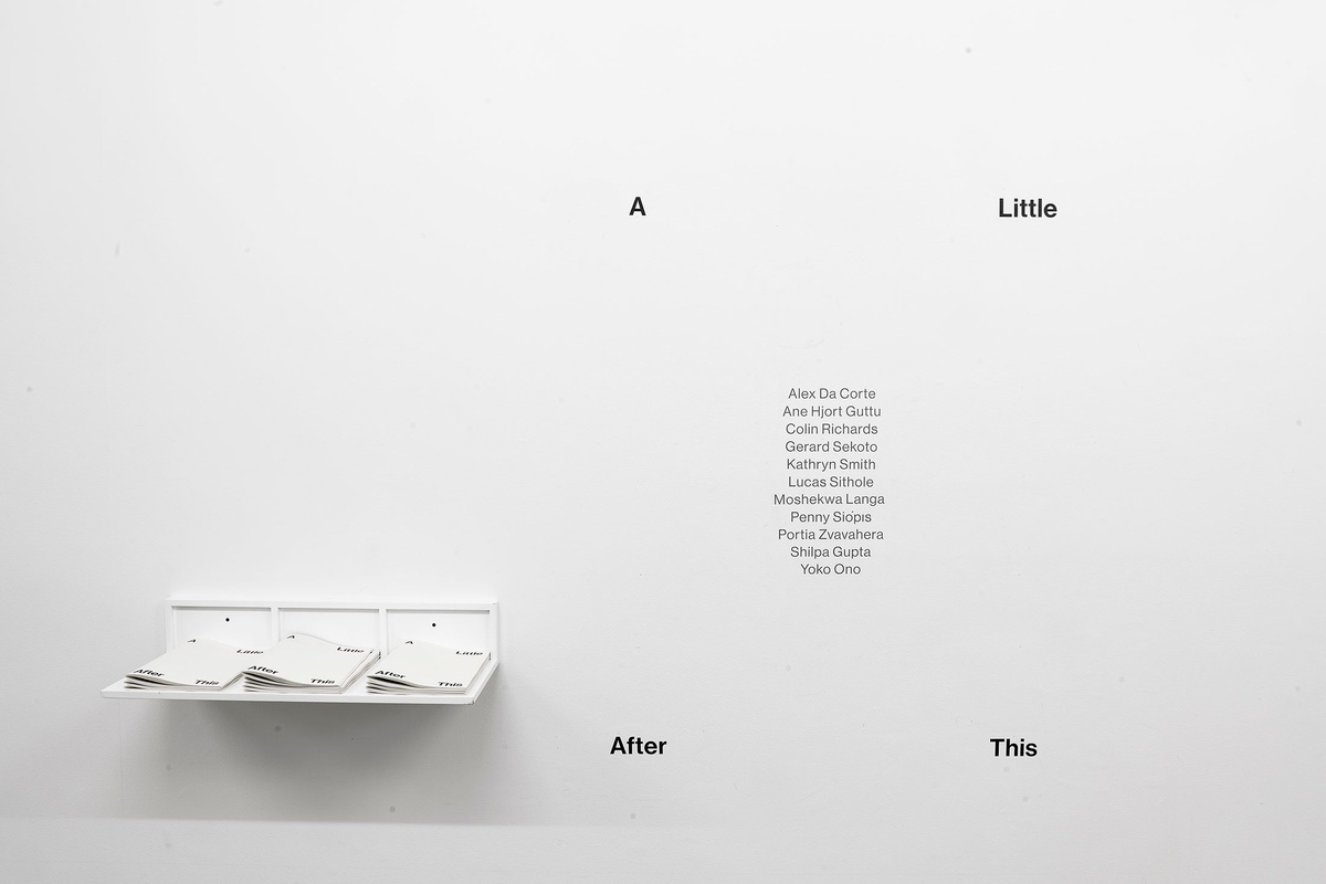 Installation photograph from the 'A Little After This' exhibition in A4 Arts Foundation's gallery. On the left, a white wall-mounted shelf with stacks of exhibition wayfinders. On the right, the exhibition title and participating artists described on the wall in vinyl.
