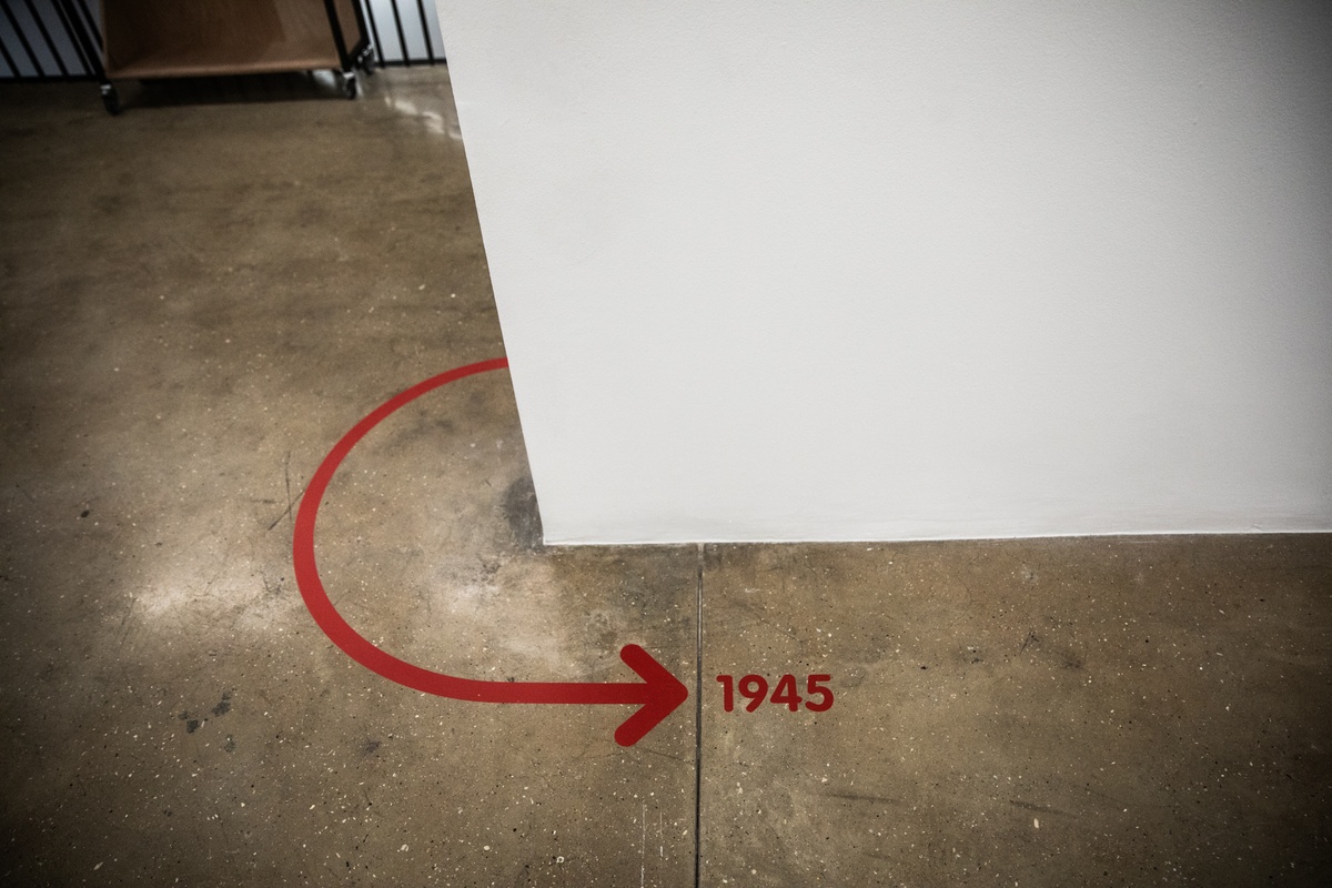 Event photograph from the opening of the Photo Book! Photo-Book! Photobook! exhibition in A4’s Gallery in an area used to house photobooks from the years 1945 to 1967. A red floor vinyl marker features an arrows and the date ‘1945’.
