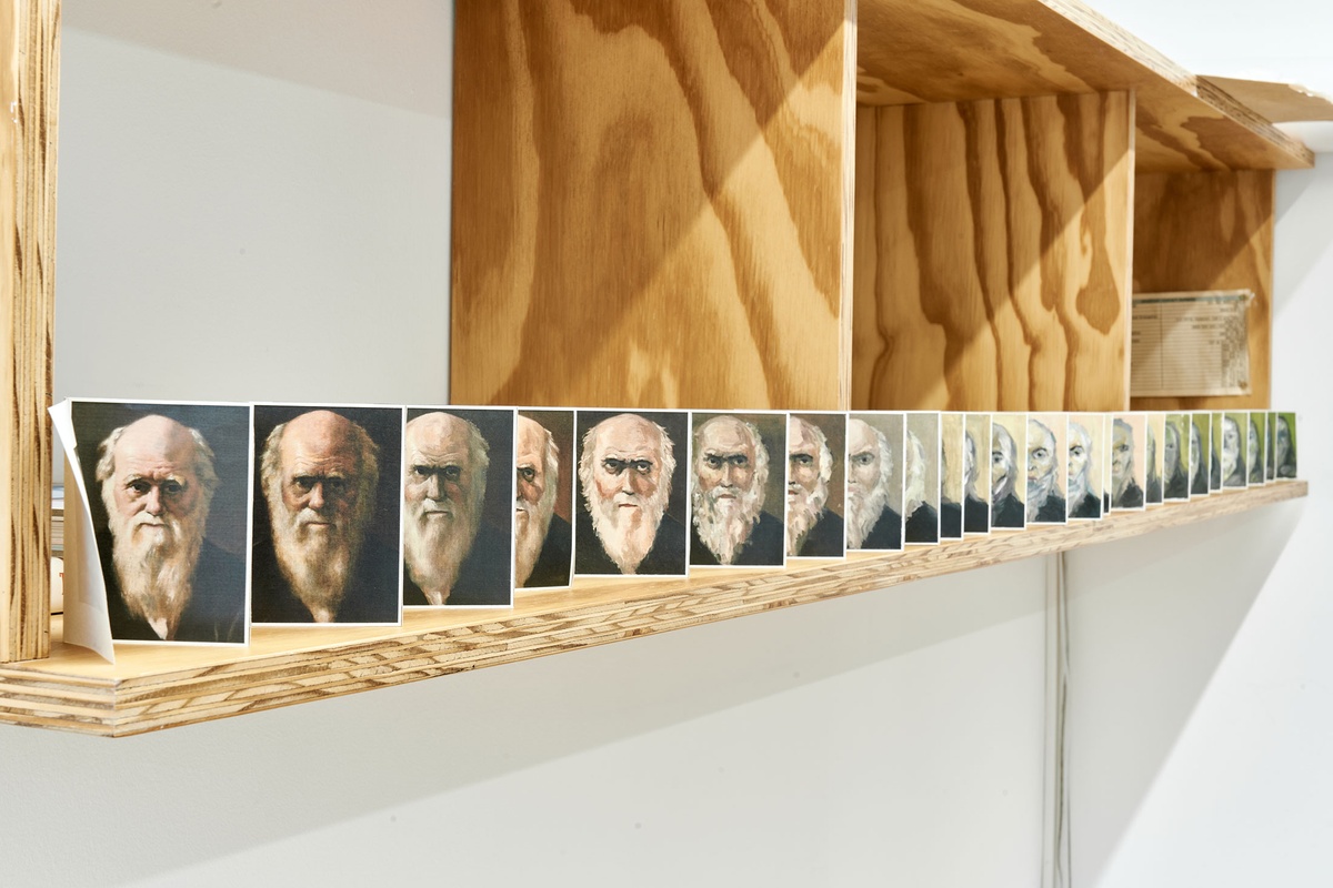 Process photograph from Patrick Waterhouse's 2022 residency in A4 Arts Foundation's studio shows a long wall-mounted shelving unit that features a paper accordion with photographic prints.
