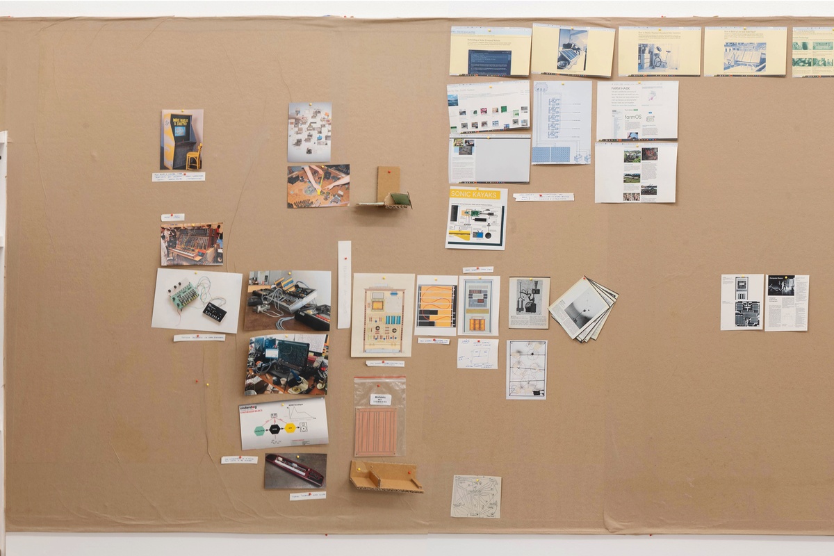 Installation photograph from Mitchell Gilbert Messina's residency in A4 Art Foundation. A wall-mounted strip of cardboard hosts pinned research notes.
