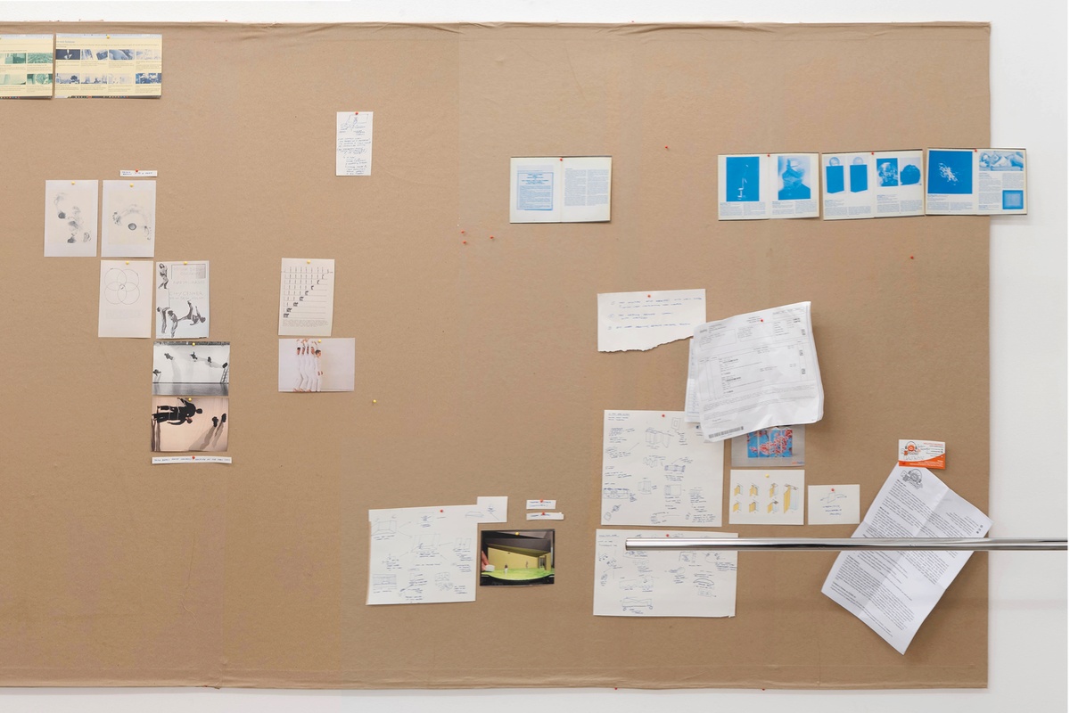 Installation photograph from Mitchell Gilbert Messina's residency in A4 Art Foundation. A wall-mounted strip of cardboard hosts pinned research notes.
