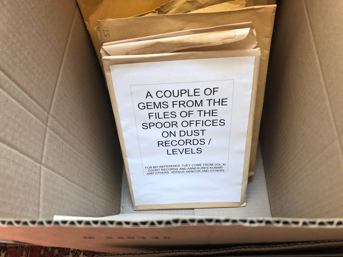 Process photograph from the ‘Picture Theory’ exhibition in A4’s Gallery that pictures a box filled with manila envelopes. The lead envelope has a label with a title that reads “A couple of gems from the files of the Spoor offices on dust records/levels,” and a subtitle that read “For my reference they come from vol XI court records and annexures Kubari and others versus Gencor and others.”
