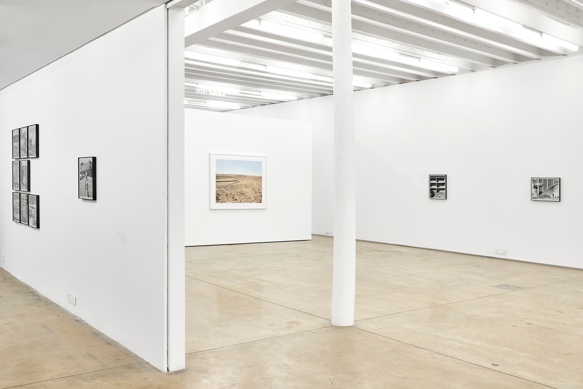 Installation photograph from the ‘Picture Theory’ exhibition in A4’s Gallery. On the left, monochrome photographs from David Goldblatt’s ‘In Boksburg’ series are mounted on the gallery wall. In the middle, Goldblatt’s photograph ‘The sports field, Merweville’ is mounted on the gallery wall. On the right, two of Goldblatt’s monochrome photographs are mounted on the gallery wall.
