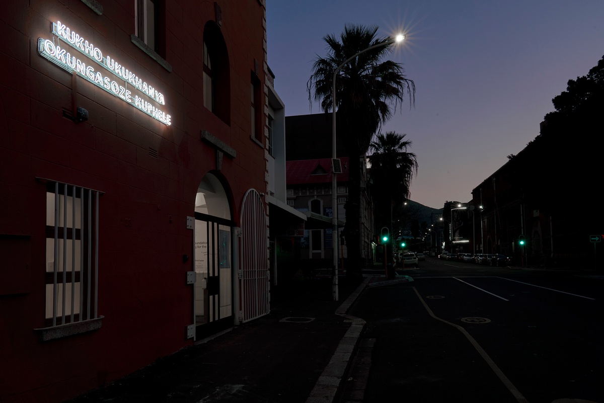 Installation photograph that shows James Webb's neon sign 'There Is A Light That Never Goes Out (isiXhosa)' mounted on A4's facade at night.
